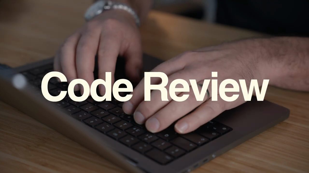 Chữ Code Review lớn chạy trên hình hai bàn tay đang gõ phím laptop