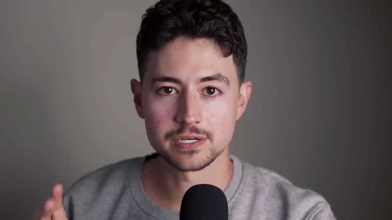 Nick Saraev nói trước camera, áo xám, micro đen phía trước