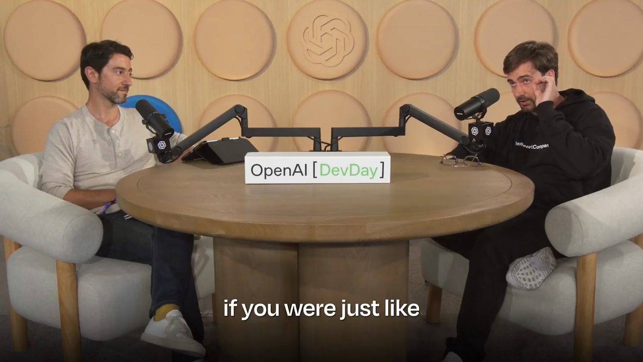 Toàn cảnh hai người ngồi đối diện ở bàn tròn có biển OpenAI DevDay