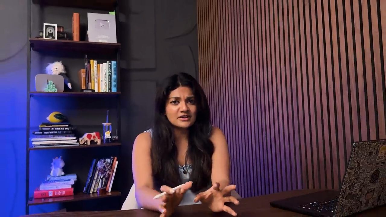 Aishwarya Srinivasan nói trước camera, phía sau là kệ sách và bức tường ốp gỗ
