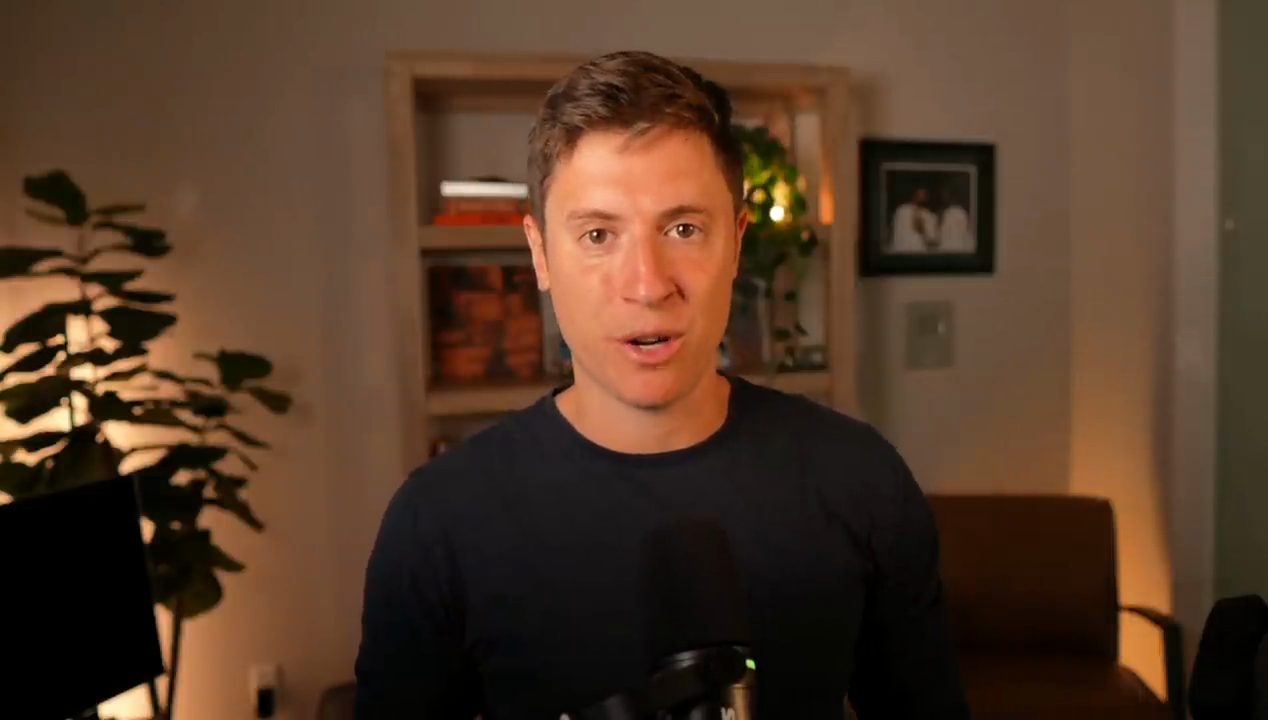Alex Finn nói trước camera trong phòng làm việc có giá sách